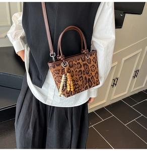Detail of leopard print bucket bag with brown handles and a wooden bead tassel charm