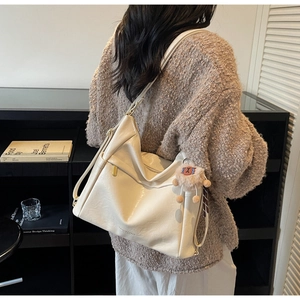 Detail of off-white faux leather tote bag with metal zipper and plush charm accessory