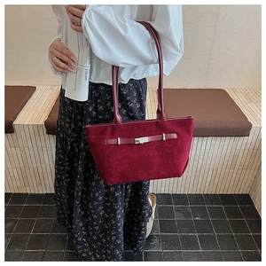 Detail of burgundy suede tote bag with metal buckle strap on a minimalist wooden chair