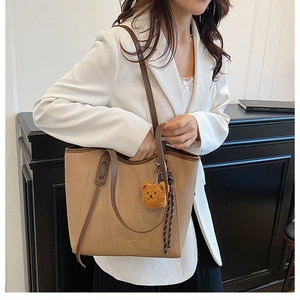 Detail of khaki lychee grain leather tote bag with cute bear charm and woven drawstring