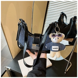 Detail of crescent denim bag with glossy leather, silver hardware and cute bear charm