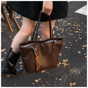 Dettaglio della borsa tote in pelle caffè scuro con ciondolo decorativo a nappa intrecciata