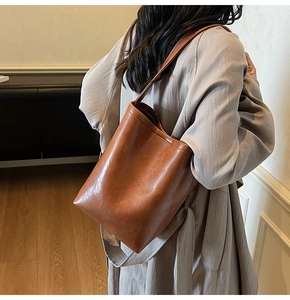 Caramel brown bucket bag shown on shoulder in a warm minimalist indoor setting