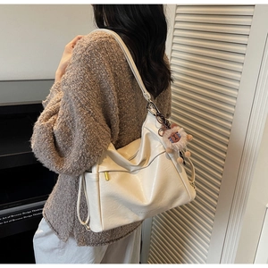 Side view of cream hobo shoulder bag with plush pendant on a model in a modern room
