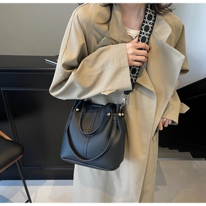 Détail du sac seau noir en cuir grainé avec une large bandoulière géométrique