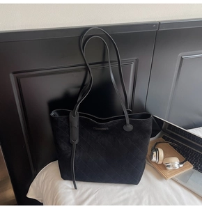 Close-up of black quilted suede tote bag with diamond stitching and long shoulder straps