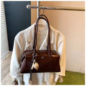 Detail of dark brown glossy Boston bag with letter logo and a baseball charm on the handle
