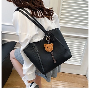 Detail of black pebbled leather tote bag featuring a cute brown plush bear charm