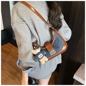 Detail of vintage denim and leather shoulder bag with decorative teddy bear pendant