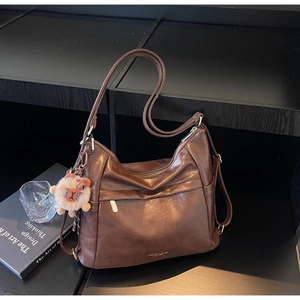 Detail of a large brown leather tote bag featuring a cute plush bear charm on the side