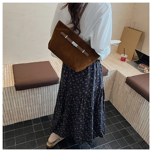 Brown suede tote bag detail featuring leather strap and metal buckle in lifestyle setting
