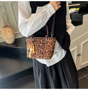 Close-up of leopard print bucket bag with brown leather handles and wood bead charm