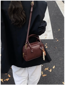 Deep brown retro bowling bag with vintage bead charm worn in a street fashion style