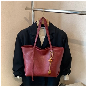Dettaglio della borsa tote rosso scuro con nappa etnica su una giacca nera