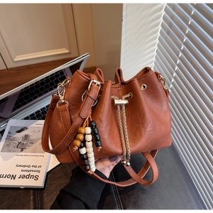 Brown leather drawstring bucket bag with beaded charm detail in a casual lifestyle setting