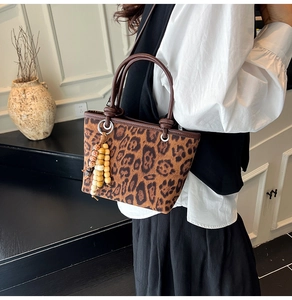 Close-up of leopard print bucket bag with leather handles and decorative wood bead tassel