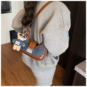 Detail of denim and leather crescent bag featuring a stylish teddy bear charm pendant