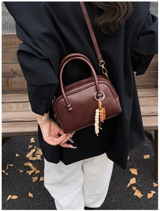 Détail du sac bowling en cuir marron foncé avec breloques perlées sur un banc