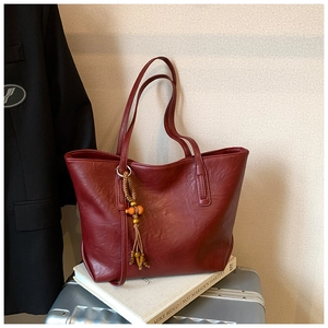 Dettaglio borsa tote in pelle rosso vino con nappa boho in legno sulla valigia