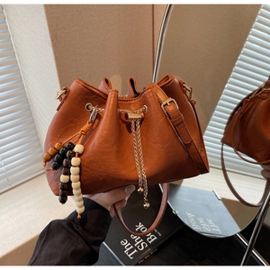 Detail of caramel bucket bag featuring lychee texture, chain drawstring and wooden beads