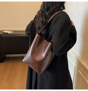Detailed texture of dark brown faux leather tote bag worn by model in suit