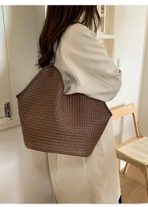 Detail view of a woven brown tote bag with leather piping and a stylish shoulder strap