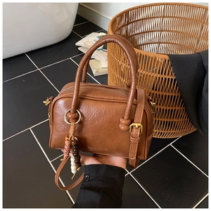 Detail of a brown leather bowling bag showing its texture, golden metal buckle and bead charm