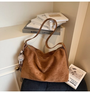 Détail d'un sac hobo en daim marron avec fermeture éclair et breloque en peluche blanche