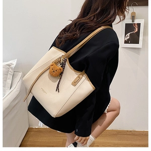 Detail view of beige tote bag with brown straps, striped ribbon, and cute bear pendant