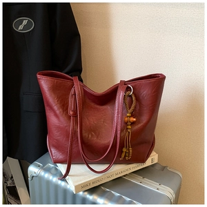 Dettaglio borsa tote vintage rosso scuro con nappa in legno su una valigia argento