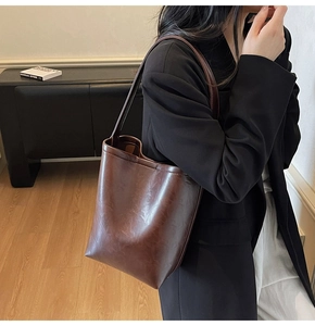 Close-up of deep brown bucket tote bag with vintage wrinkled leather texture and slim strap
