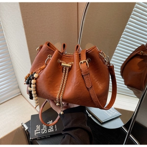 Detail of a brown leather bucket bag with a gold chain drawstring and beaded charm