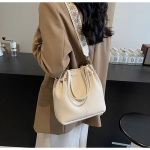 Gros plan du sac seau en cuir blanc cassé avec bandoulière géométrique large et rivets