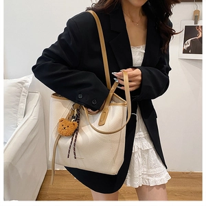 Detail of cream tote bag with brown contrast trim and cute teddy bear charm accessory
