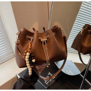 Detail of brown leather bucket bag featuring gold chain drawstring and beaded charms