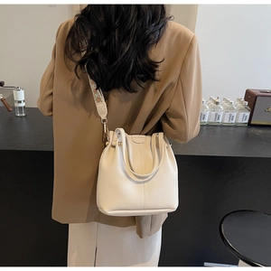 Modèle portant un sac seau en cuir blanc cassé avec une large bandoulière à motifs