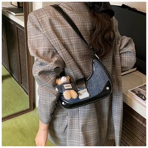 Detail of denim crescent shoulder bag with a cute teddy bear charm on model