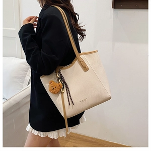 Detail of off-white lychee leather tote bag with brown straps and cute bear pendant