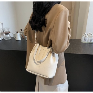 Sac seau chic en cuir beige porté en bandoulière sur un blazer de couleur camel