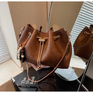 Detail of brown pleated bucket bag with drawstring closure and beaded wooden charm
