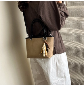 Detail of tan suede tote bag with black contrast handles and decorative wooden bead tassel