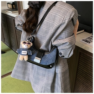 Detail of blue denim crescent bag featuring leather trim, silver buckle, and teddy charm