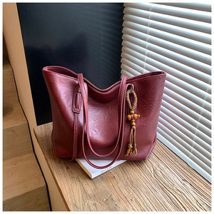 Dettaglio della borsa tote bordeaux con finitura testurizzata e ciondolo decorativo a nappa