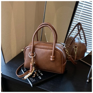 Close-up of brown faux leather bowling bag with boho bead charm and metal zipper