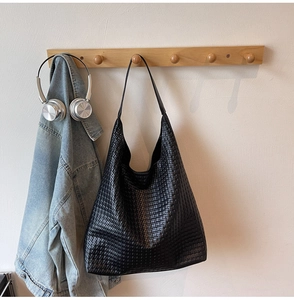 Detail of black woven leather tote bag hanging on a hook with lifestyle accessories