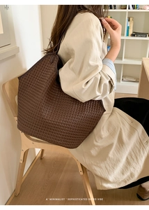 Close-up of deep brown woven leather tote bag styled with a beige trench coat