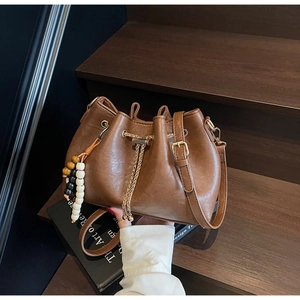 Detail of dark brown drawstring bucket bag with wooden beads and gold hardware on stairs