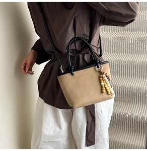 Detail of camel suede bucket bag with wooden bead tassel and black leather handles