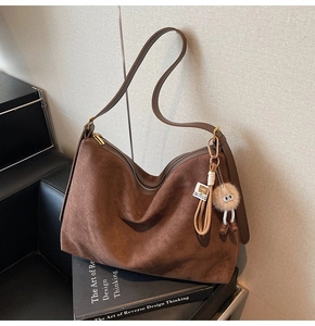 Détail d'un sac cabas en daim marron avec bandoulière en cuir et un pendentif peluche