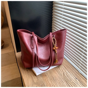 Dettaglio della borsa tote in pelle bordeaux con ciondolo di perline in legno e nappa su tavolo